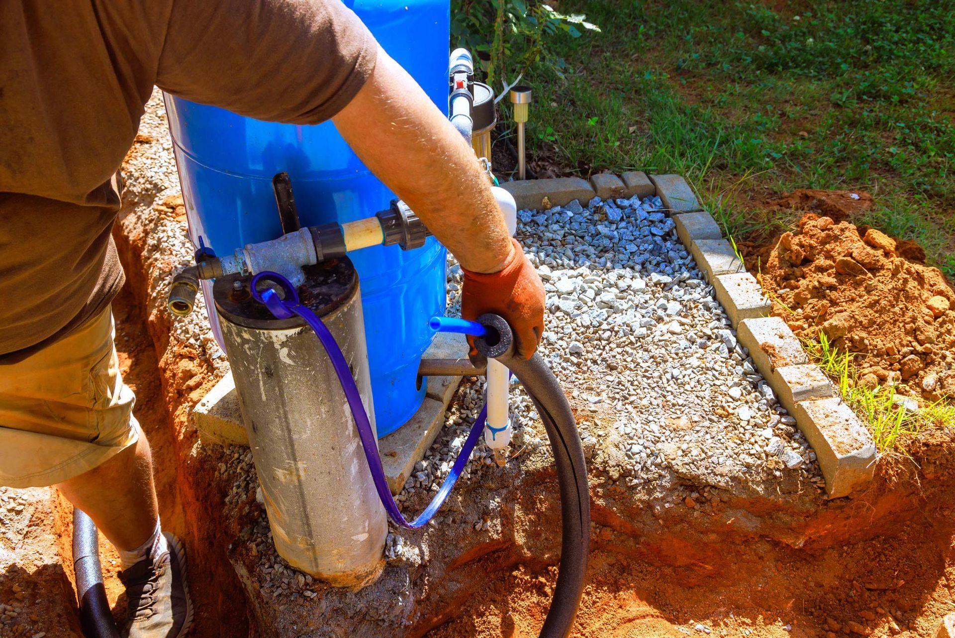 Worker repairing water pump system in residential yard during sunny afternoon.