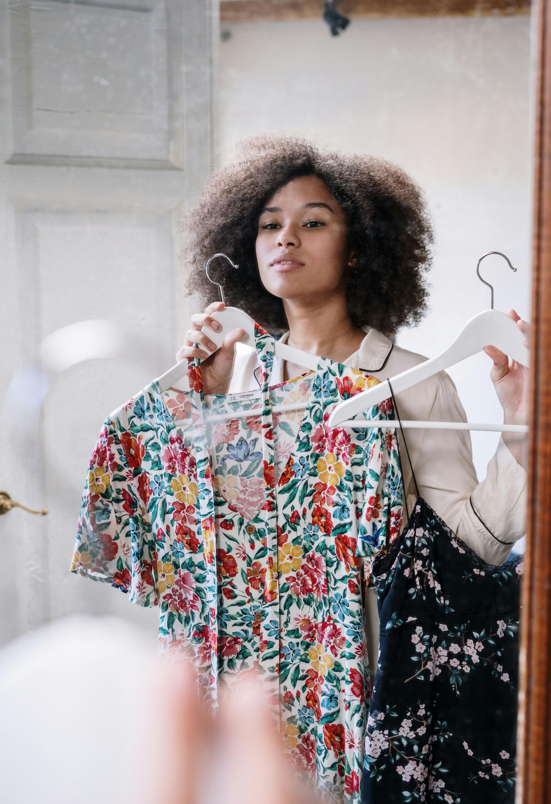 A woman is holding a floral shirt in front of a mirror.