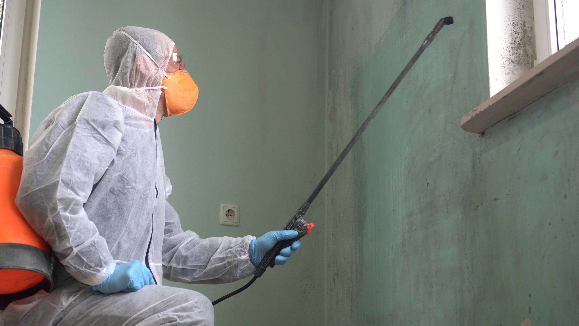 A man in a protective suit is spraying a wall with a sprayer.