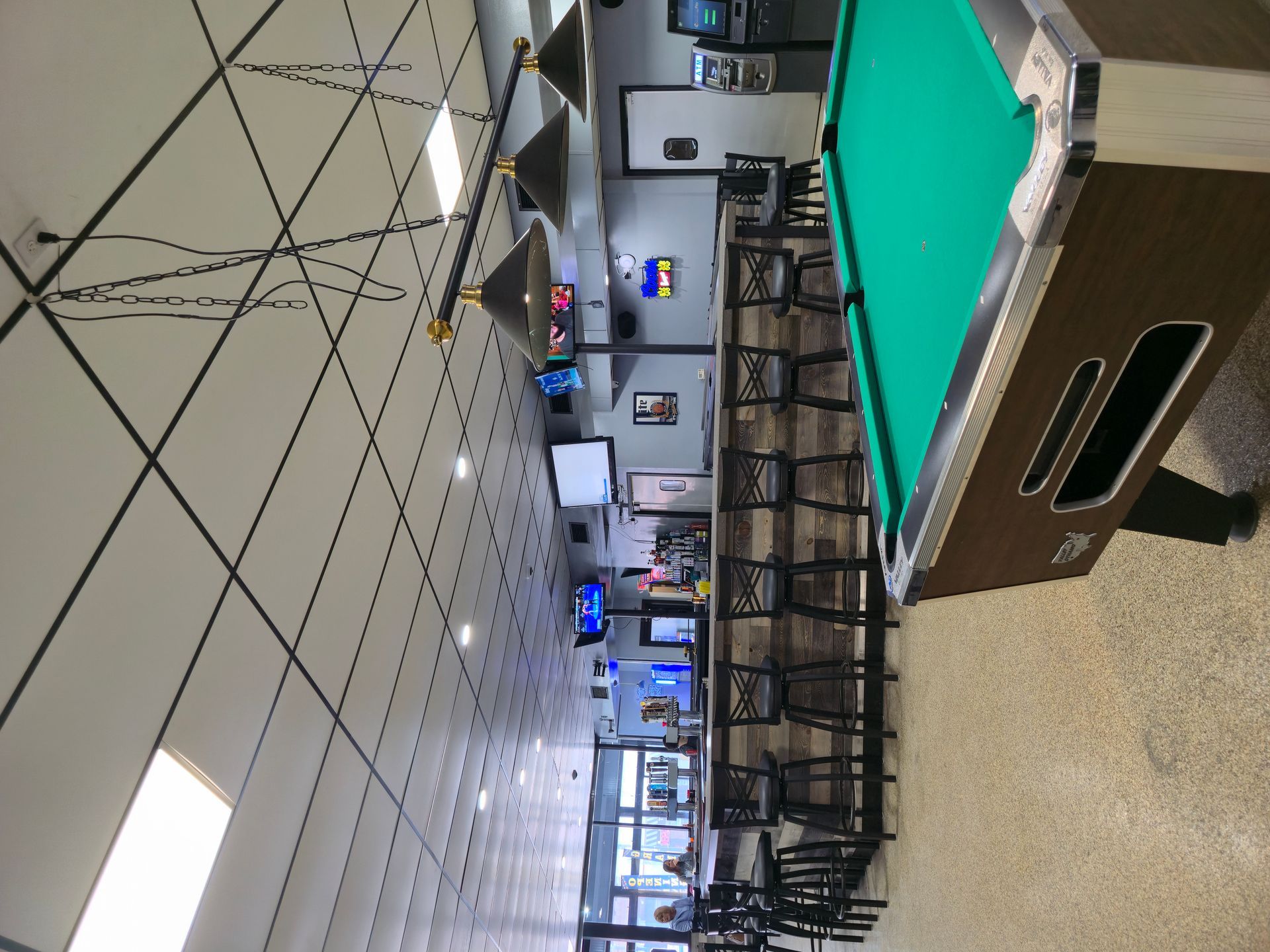 An indoor view of a game room featuring a green pool table in the foreground and a bar area with stools in the background.