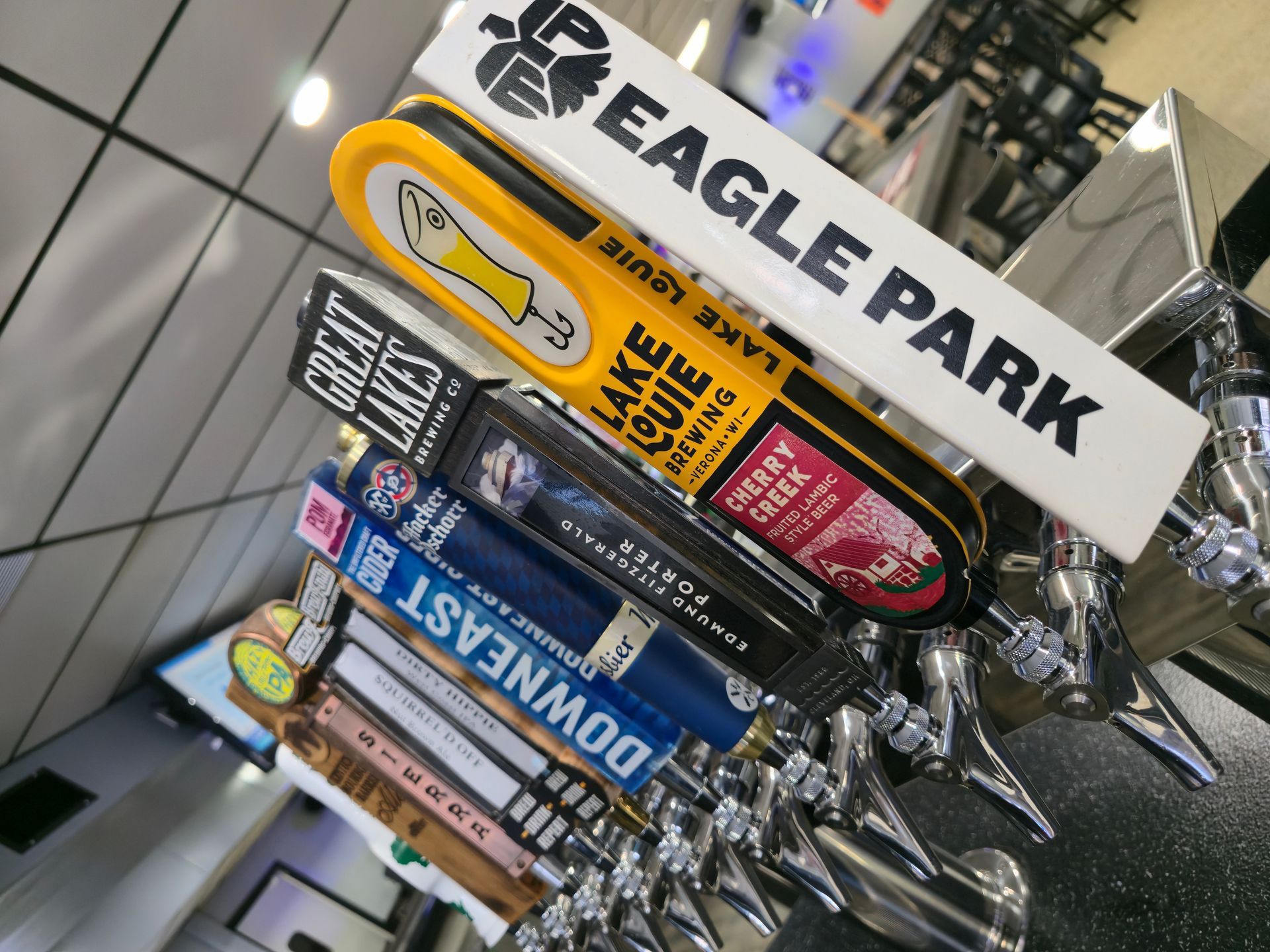 A tilted, close-up shot of a row of beer tap handles in a bar, featuring brands like Eagle Park and Lake Louie Brewing.