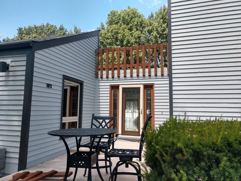Patio with black table, white siding, French doors, and wooden balcony railing under blue sky