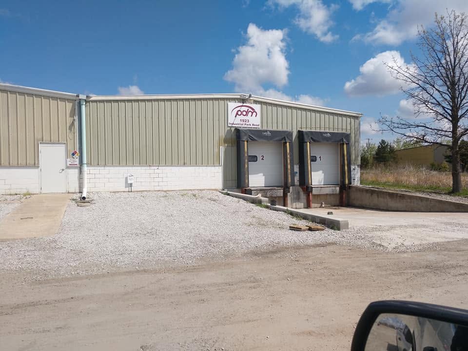 Gravel lot outside a metal industrial building with two dock doors and a partly cloudy sky