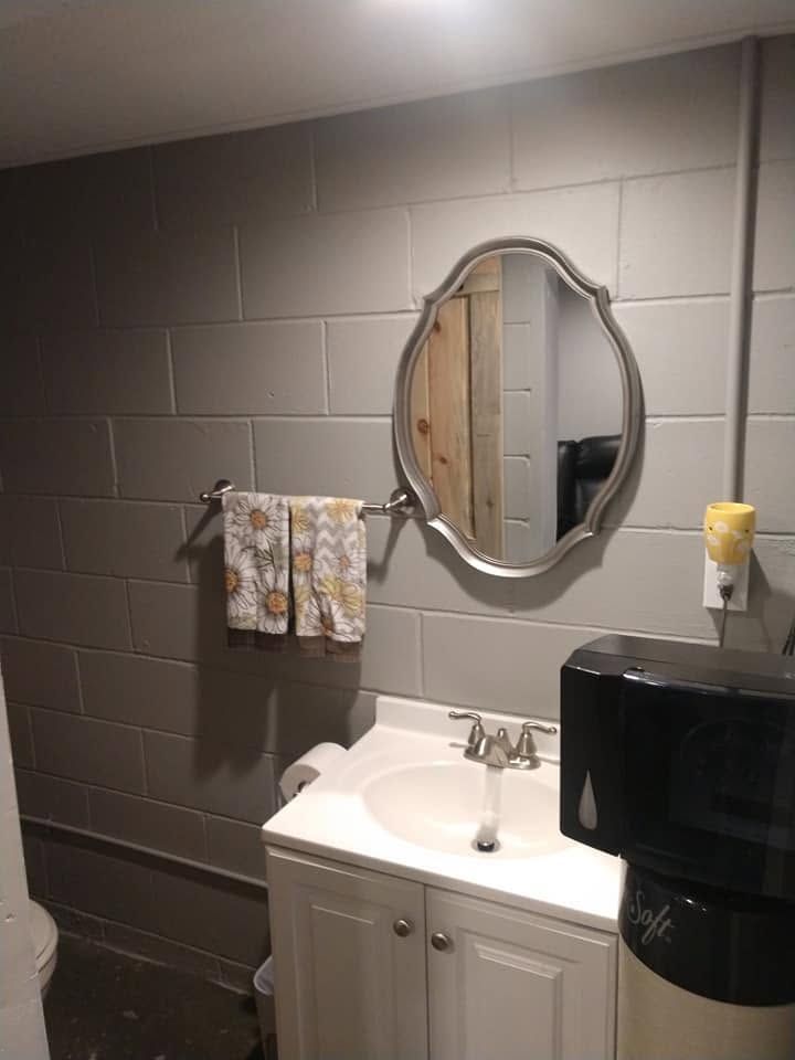 Small restroom with gray walls, white sink cabinet, oval mirror, and black paper towel dispenser.