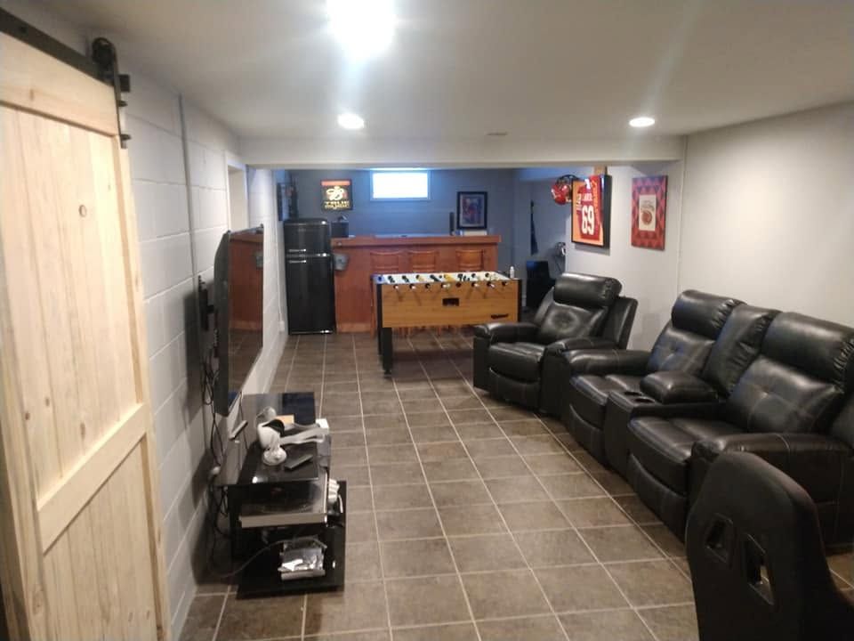 Finished basement rec room with black leather recliners, tiled floor, foosball table, and wood sliding door.