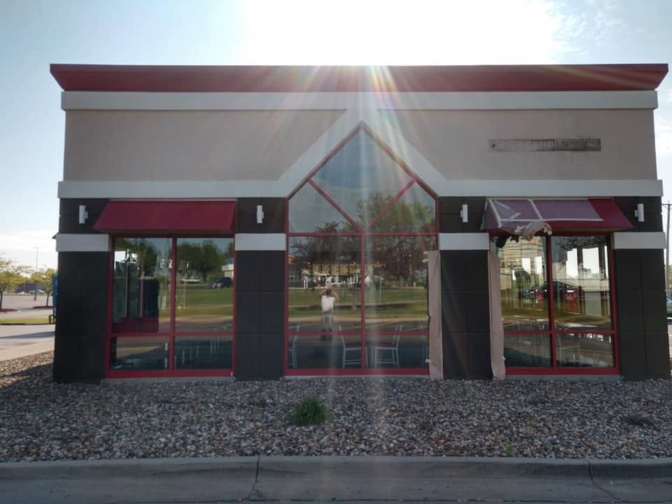 Front view of a small storefront with red awnings, beige walls, and a glass entrance in bright sunlight