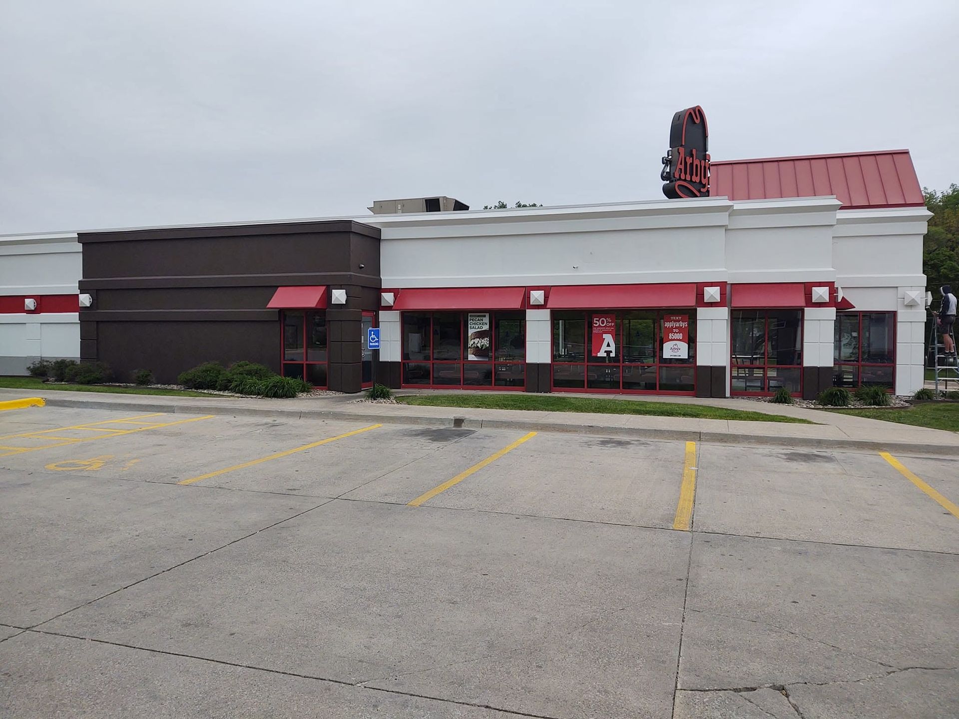 Abandoned storefront with boarded windows, red awning, and empty parking lot under cloudy sky