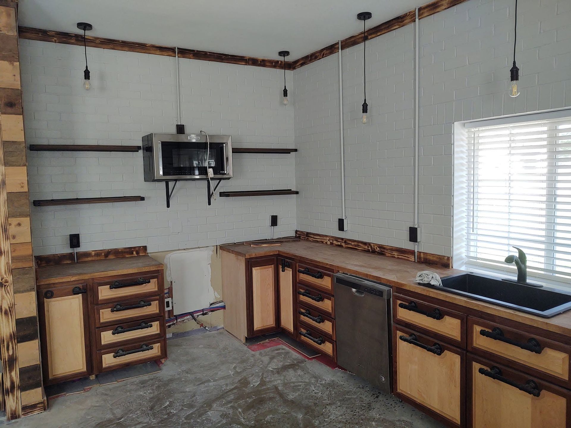 Empty kitchen with unfinished cabinets, white tile walls, open shelves, and a window over the sink.
