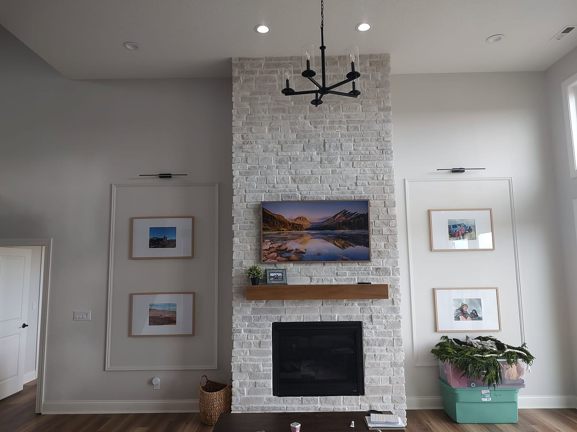 Living room with white brick fireplace, framed art, black chandelier, and potted plant by a bright window