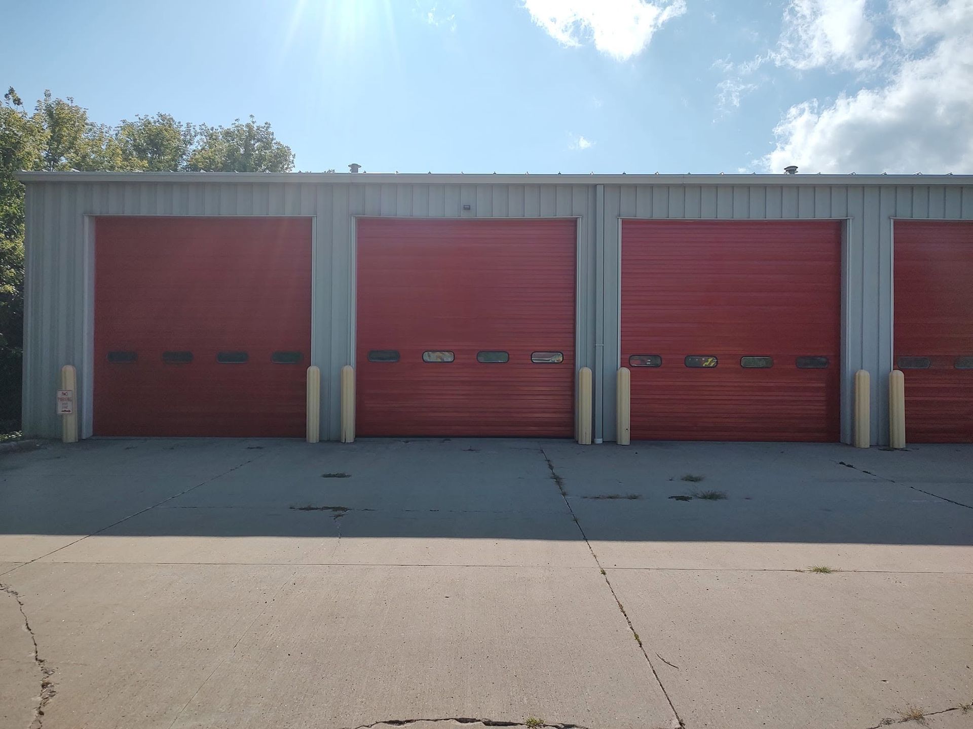 Row of red roll-up garage doors on a gray industrial building in bright sunlight