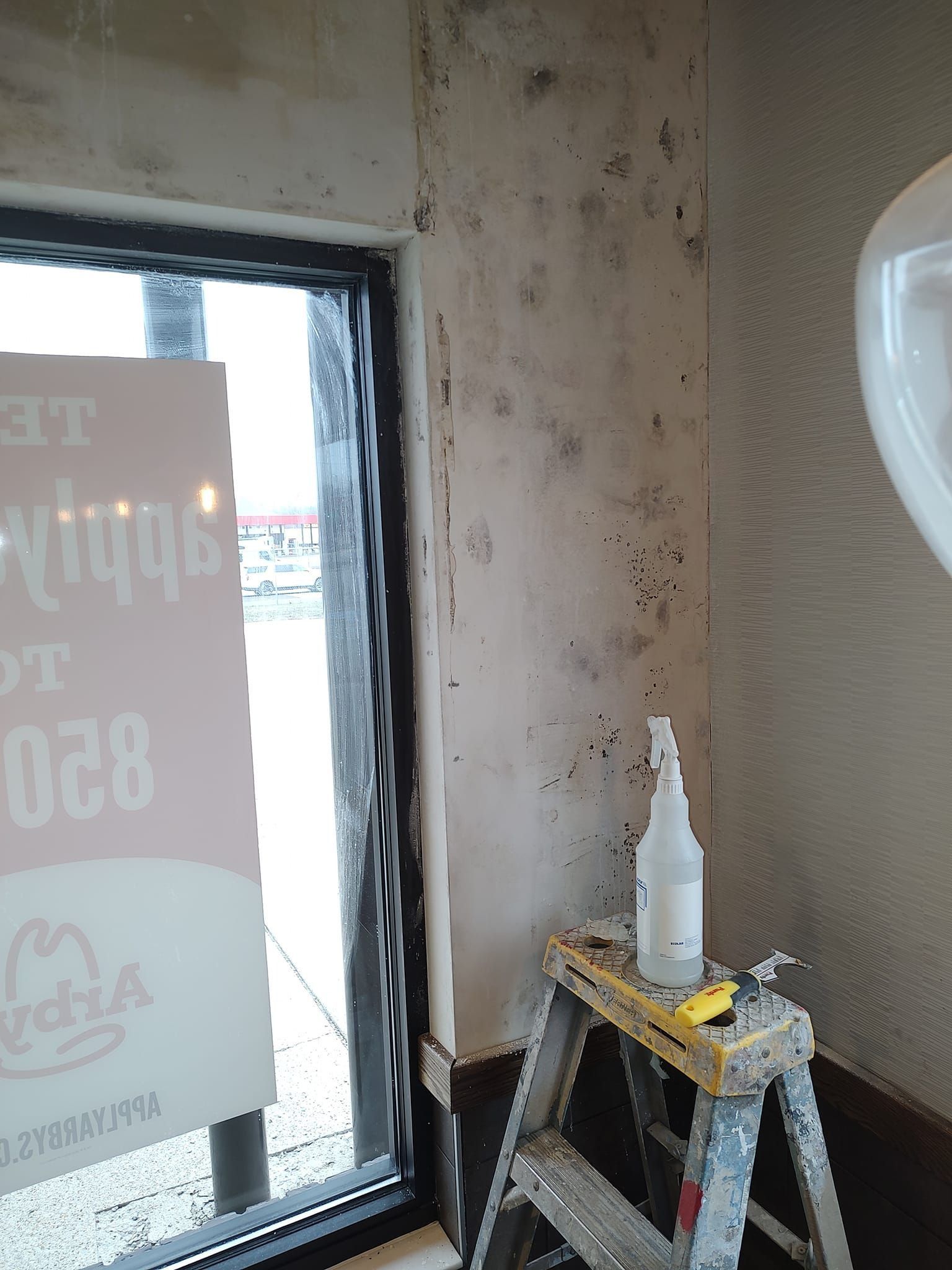 A worn interior wall with a small window and a step stool holding paint supplies.