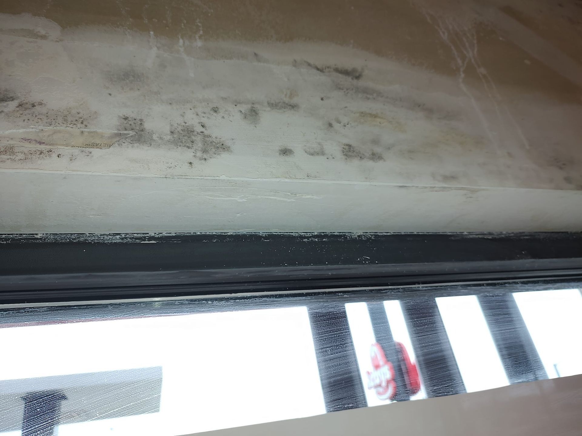 Dirty ceiling above a window with black trim and bright light outside