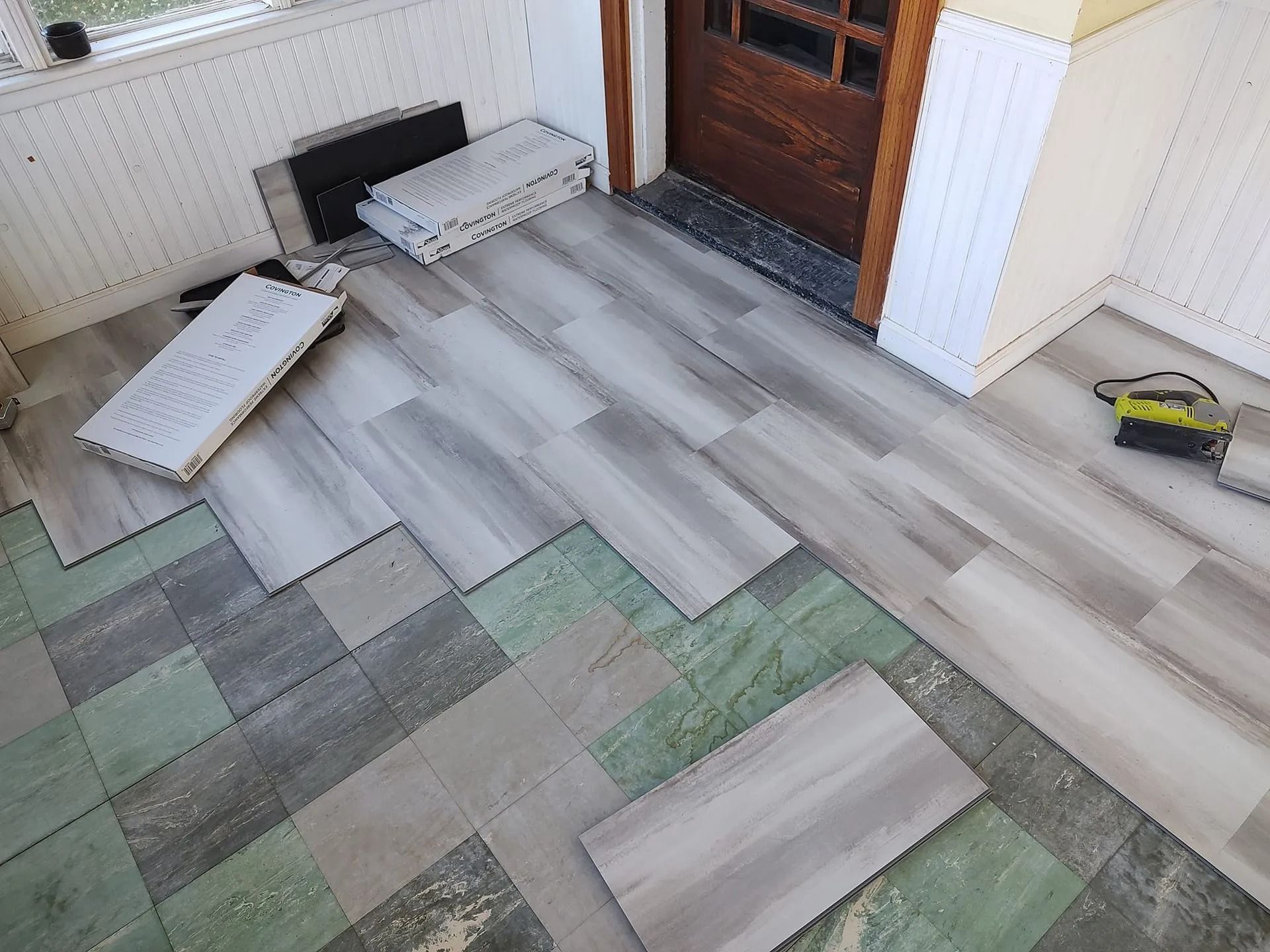 Partially installed gray wood-look flooring with loose planks in a room near a door