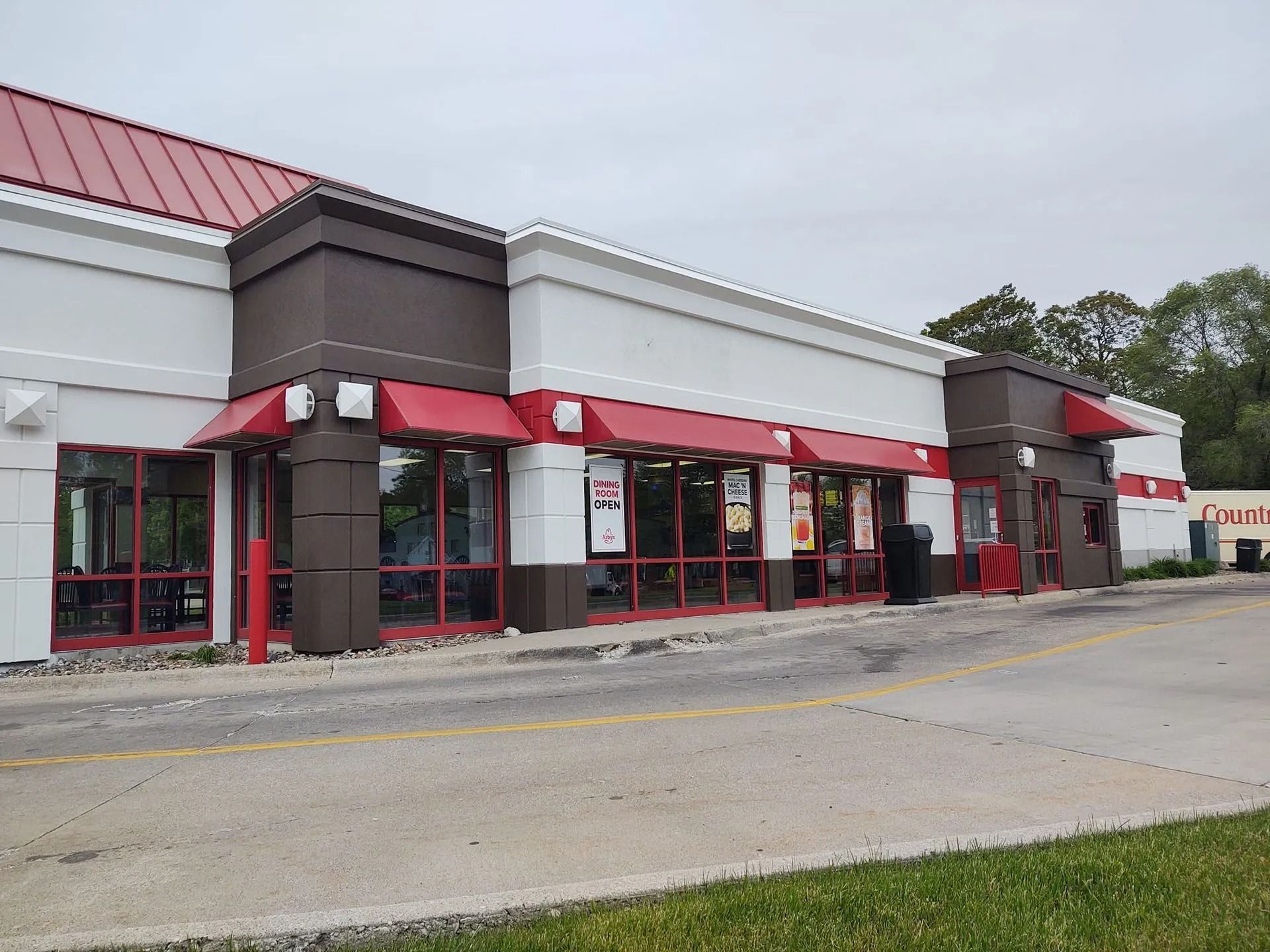 Strip mall storefront with red awnings and large windows, viewed from a parking lot.