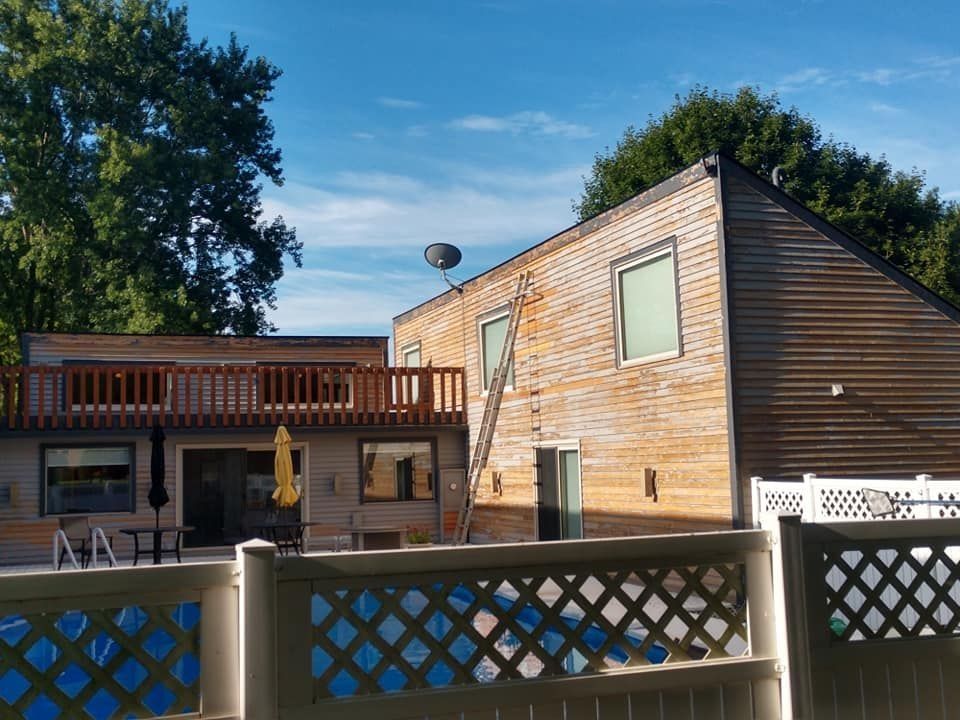 Backyard deck and two-story wooden house behind a white lattice fence under a blue sky