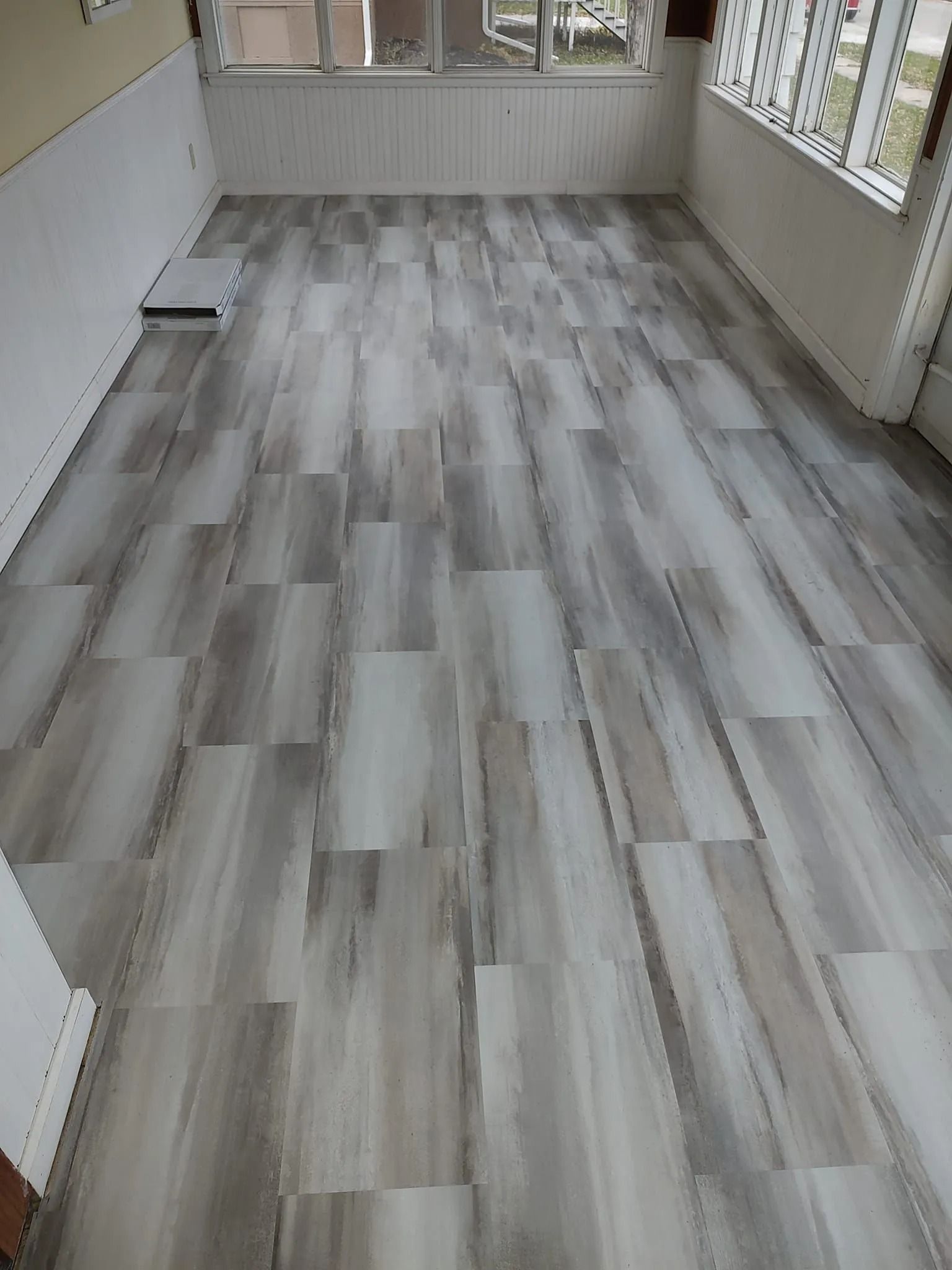 Empty room with light gray wood-look flooring and white walls, viewed from the corner toward windows.