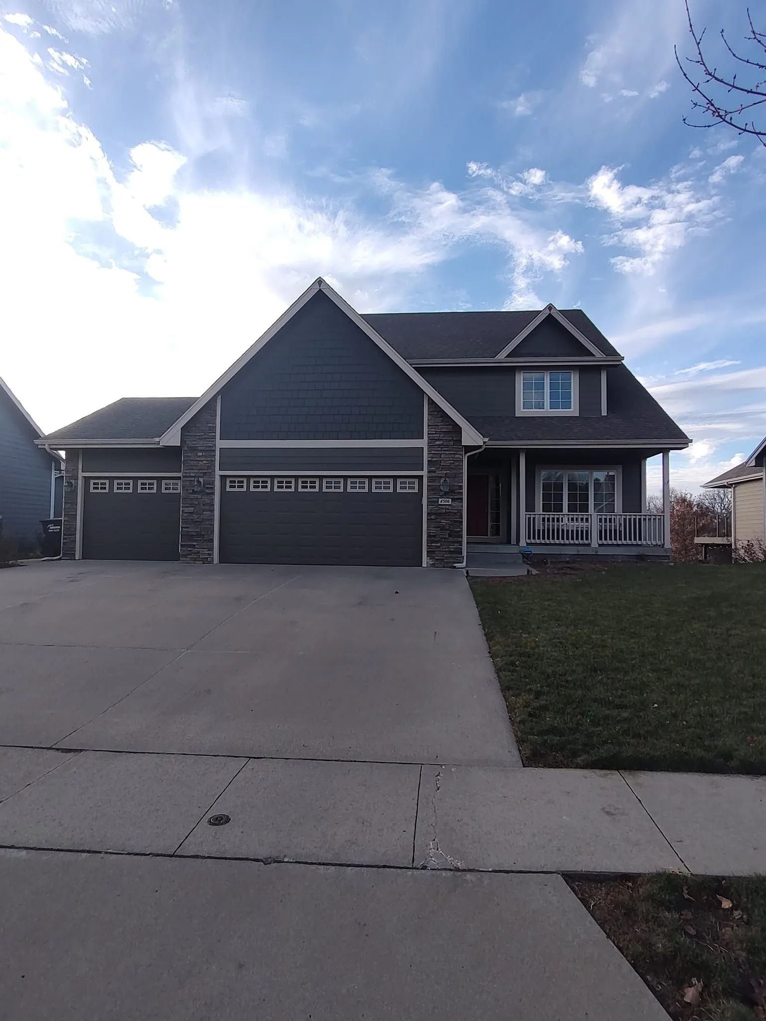 Dark gray two-story suburban house with three-car garage and wide driveway under a partly cloudy sky