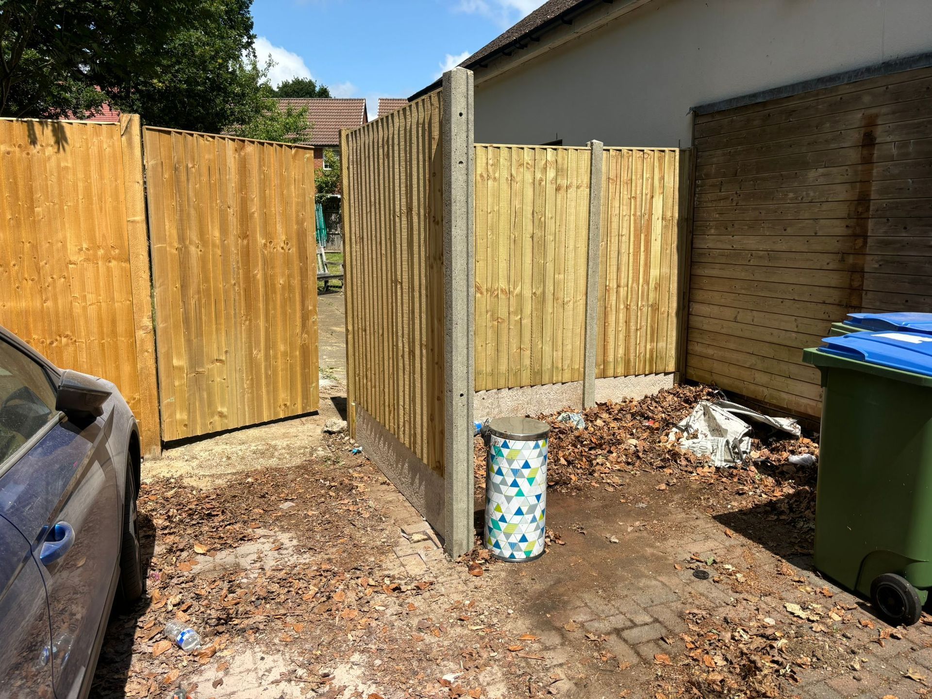 New fencing installed in garden with car and bin in foreground