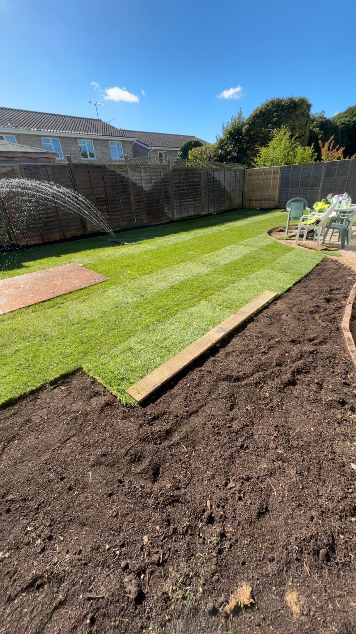 Back garden with enclosed fence and new grass being watered by a sprinkler