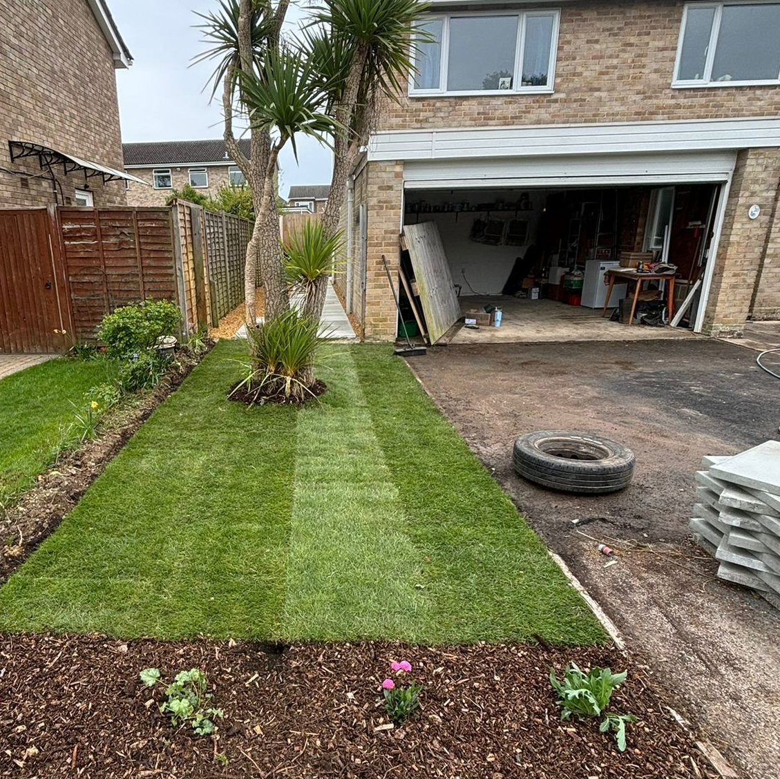 Freshly laid turf in front garden with palm trees in and house with open garage in the background
