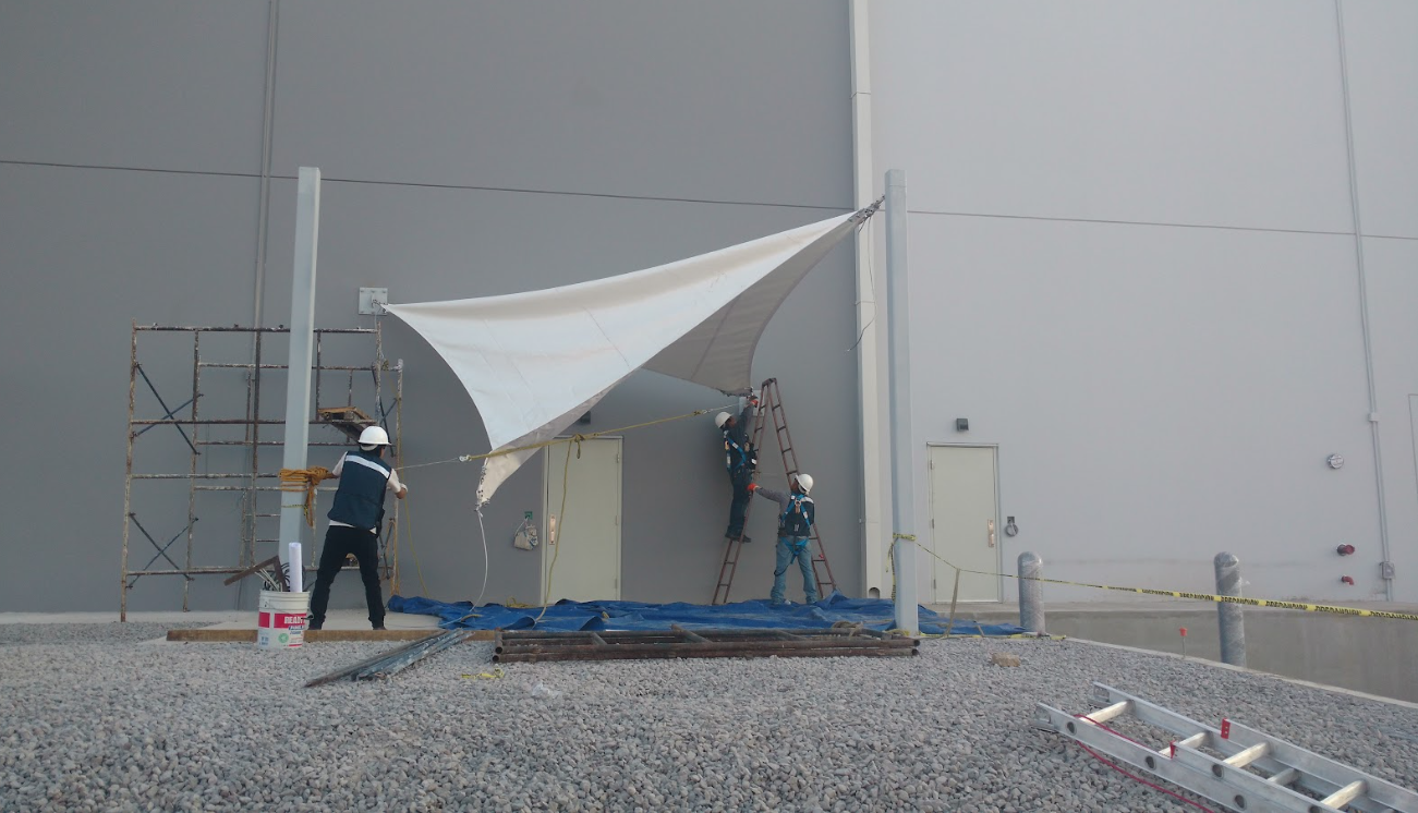 Dos trabajadores instalan una carpa blanca en una obra en construcción al aire libre de color gris.