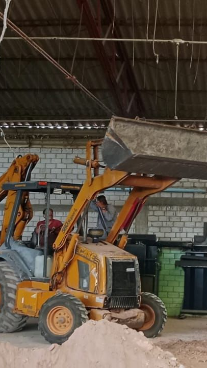 Cargadora frontal naranja con pala elevada dentro de un almacén o garaje.