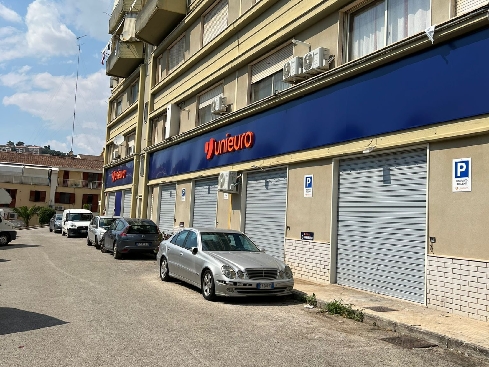 Una berlina argentata parcheggiata davanti a un edificio commerciale con facciata blu recante il logo rosso di Unieuro.