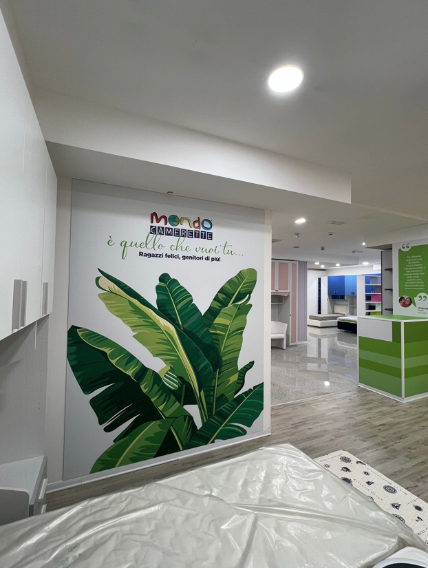 Interno di un negozio di arredamento con un murale raffigurante una foglia di banano e il logo Mondo Convenienza.