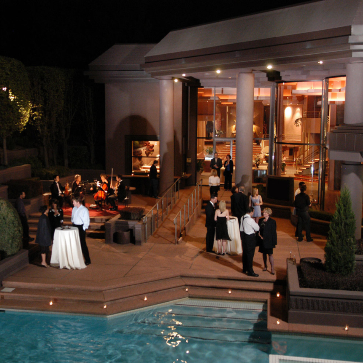 Guests mingle at a nighttime poolside patio event beside a lit modern house