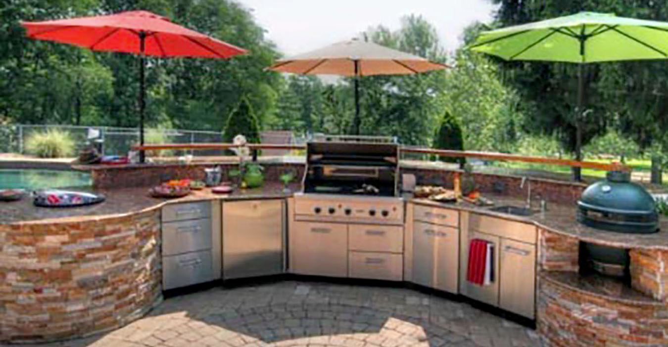 Outdoor patio kitchen with grill, sink, and brick counter under red, tan, and green umbrellas.