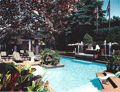 Sunlit resort pool surrounded by lounge chairs, fountains, and tropical landscaping