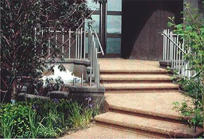 Curved stone steps leading to a front door, surrounded by lush garden plants and railings