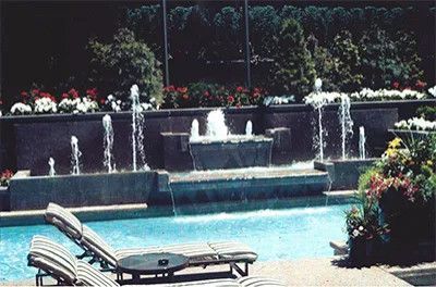 Backyard pool with a decorative fountain, lounge chairs, and colorful flowers along the edge