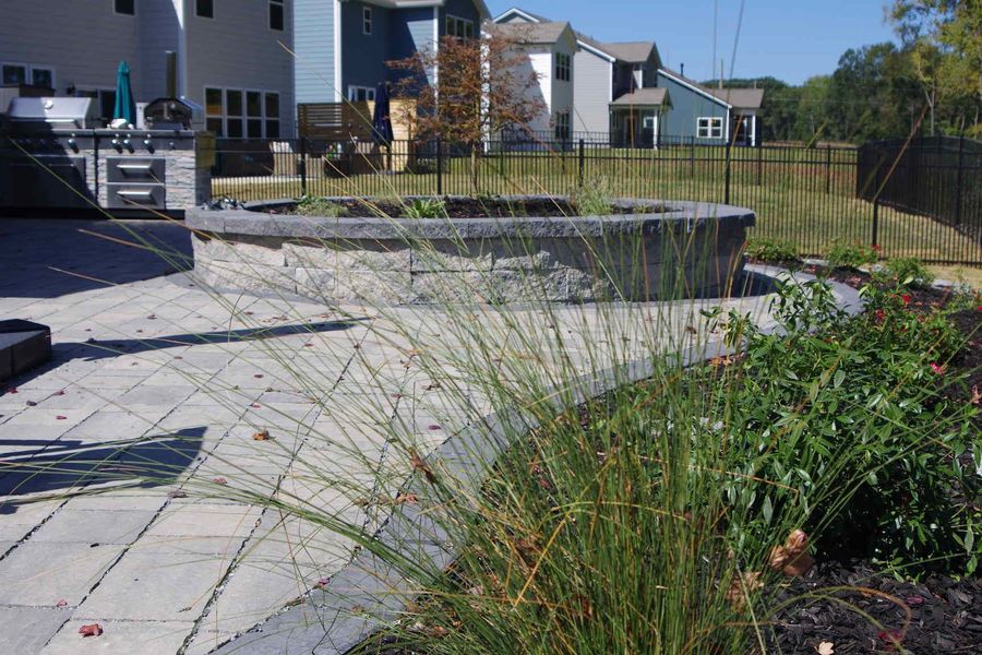 Backyard patio with stone pavers, raised planter beds, and ornamental grasses beside a house