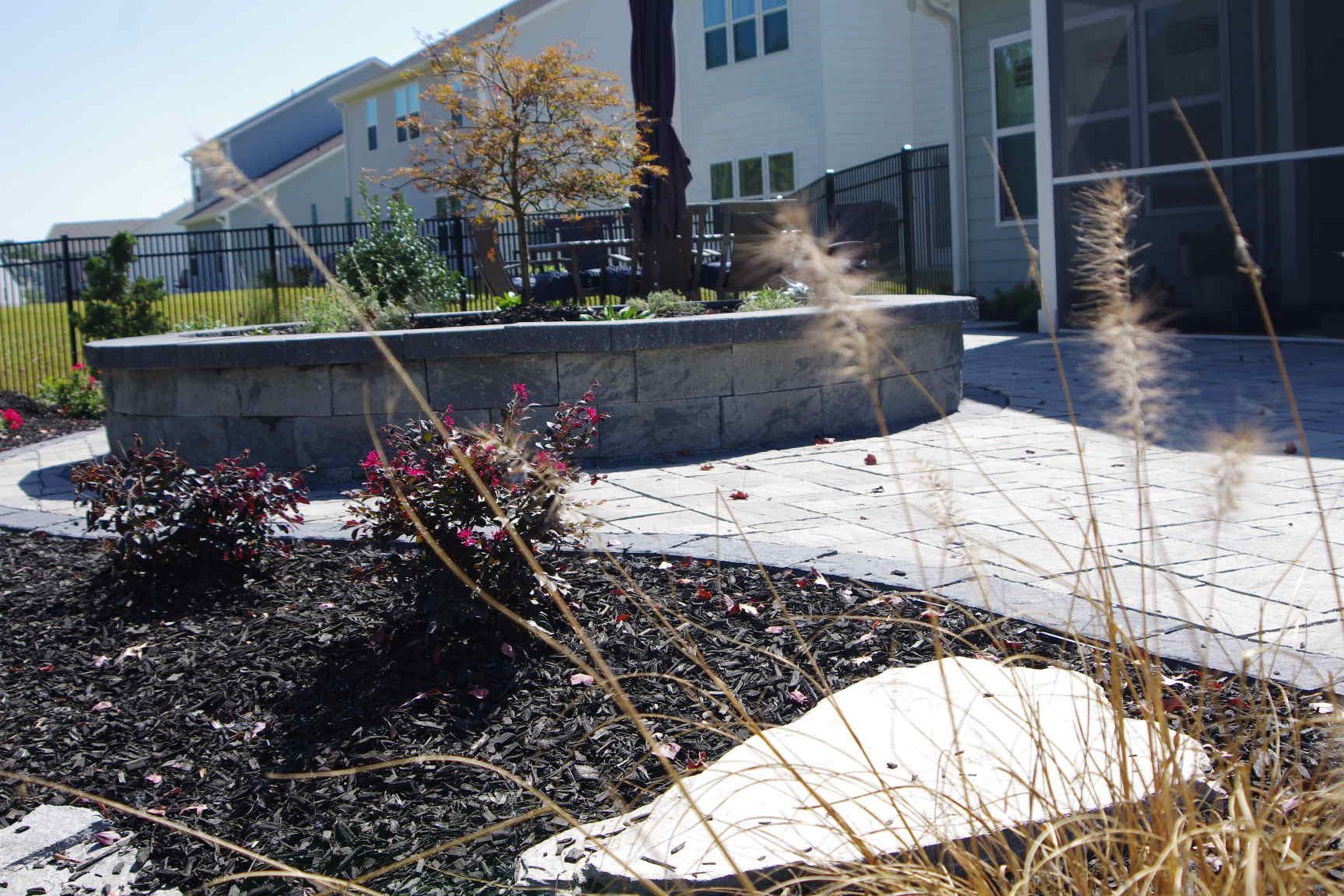 Outdoor walkway beside apartment buildings with raised stone planters and winter landscaping in sunlight