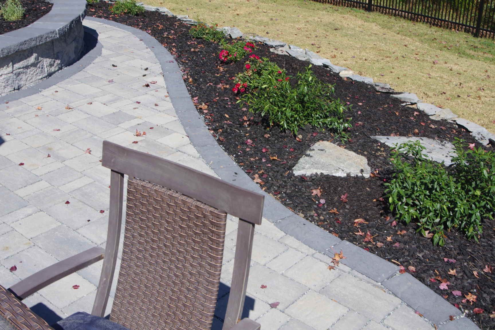 Patio with beige pavers, chair, and curved garden bed with mulch and flowers