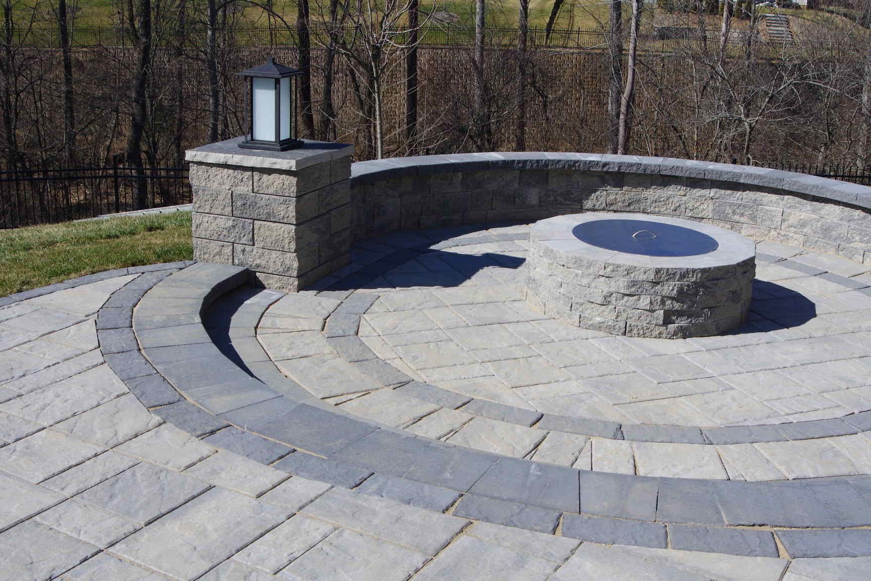 Circular stone memorial with a central bench, engraved plaque, and lantern in a paved outdoor area