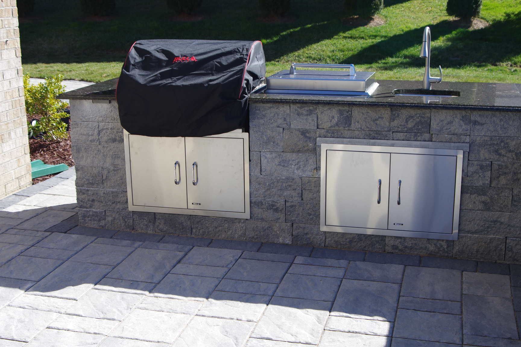 Outdoor stone patio with built-in white cabinets, sink, and a black cover on one counter