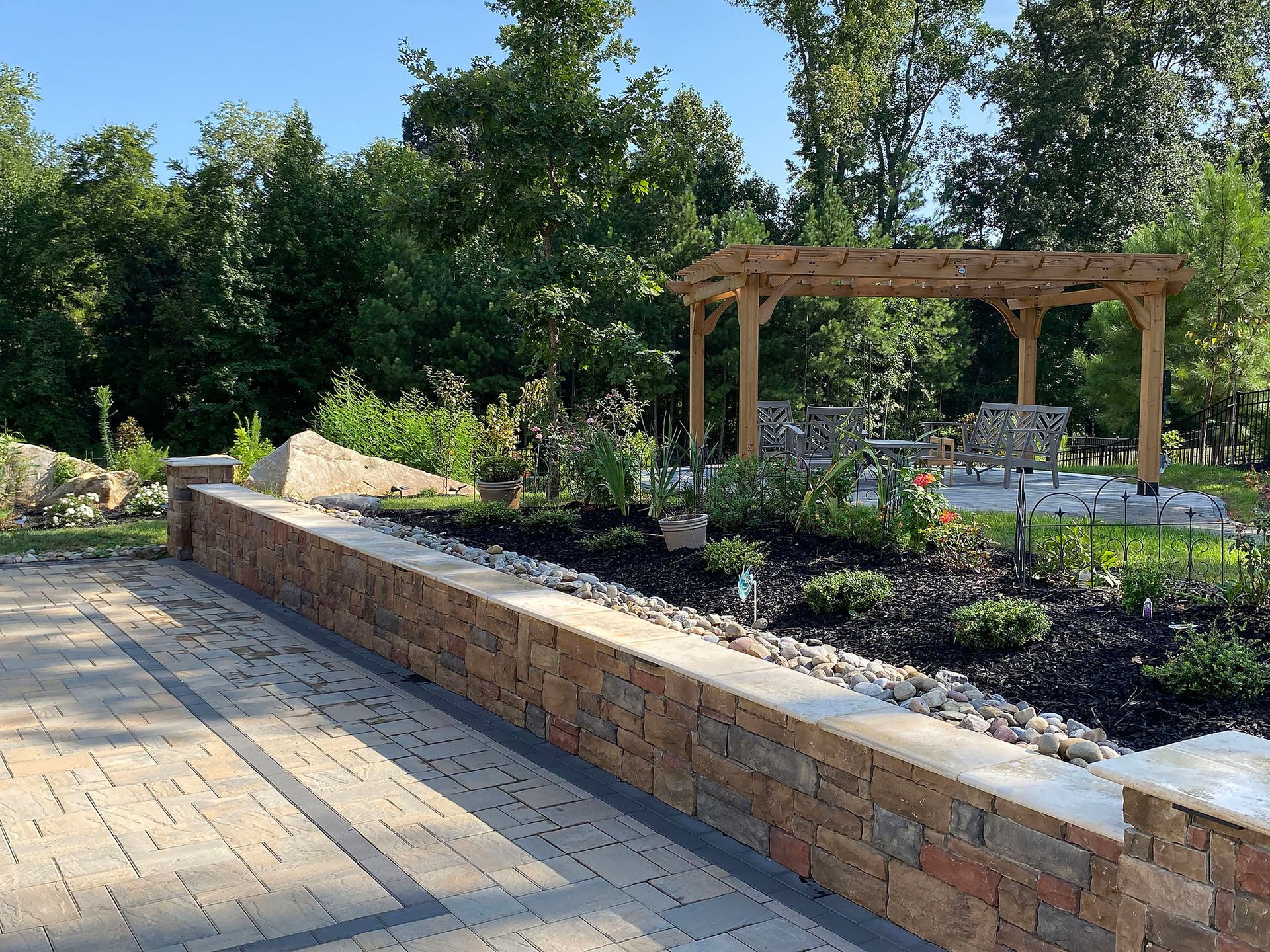 Brick patio beside a landscaped garden with trees and a wooden pergola in the background