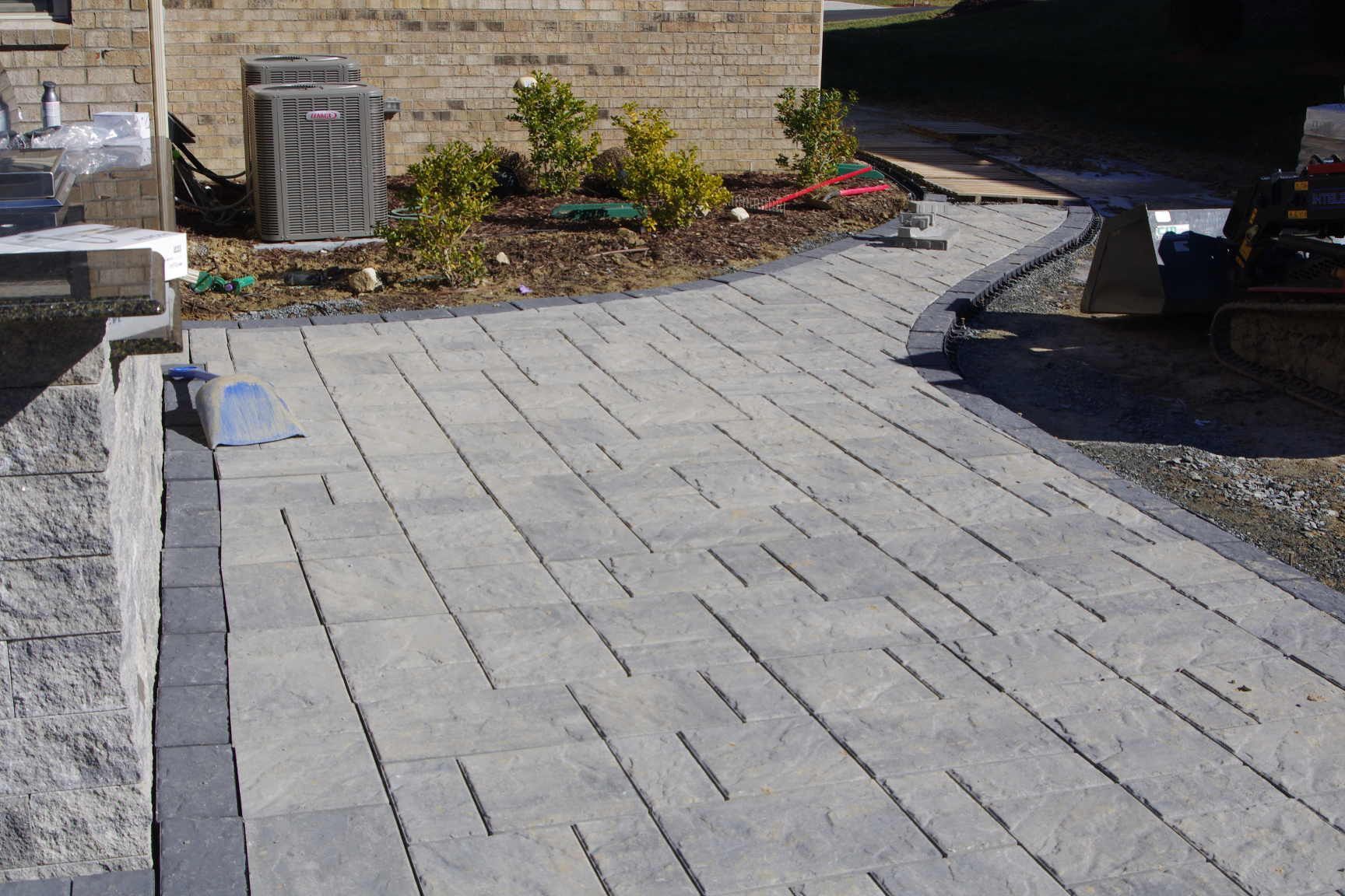 Stone-paved driveway beside a brick house and garden wall, with sunlight casting shadows