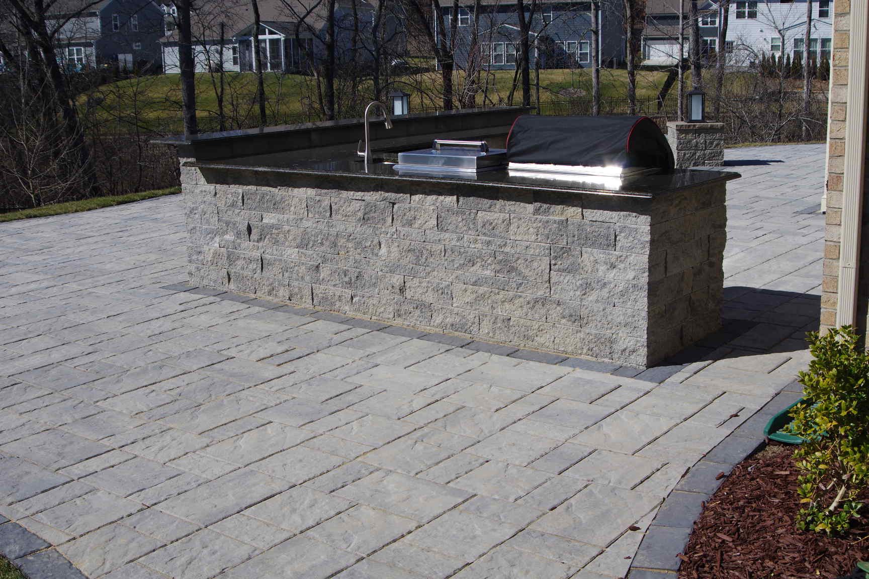 Outdoor stone drinking fountain beside a paved walkway in a sunny park.