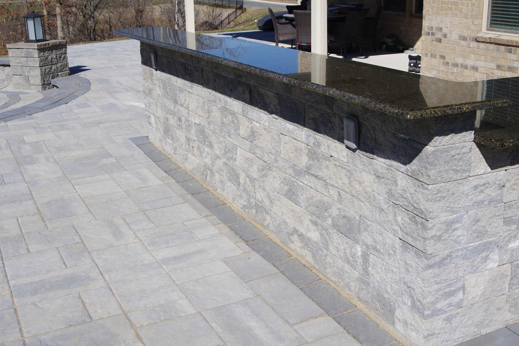 Stone patio with a low gray retaining wall and steps beside a driveway or outdoor entrance