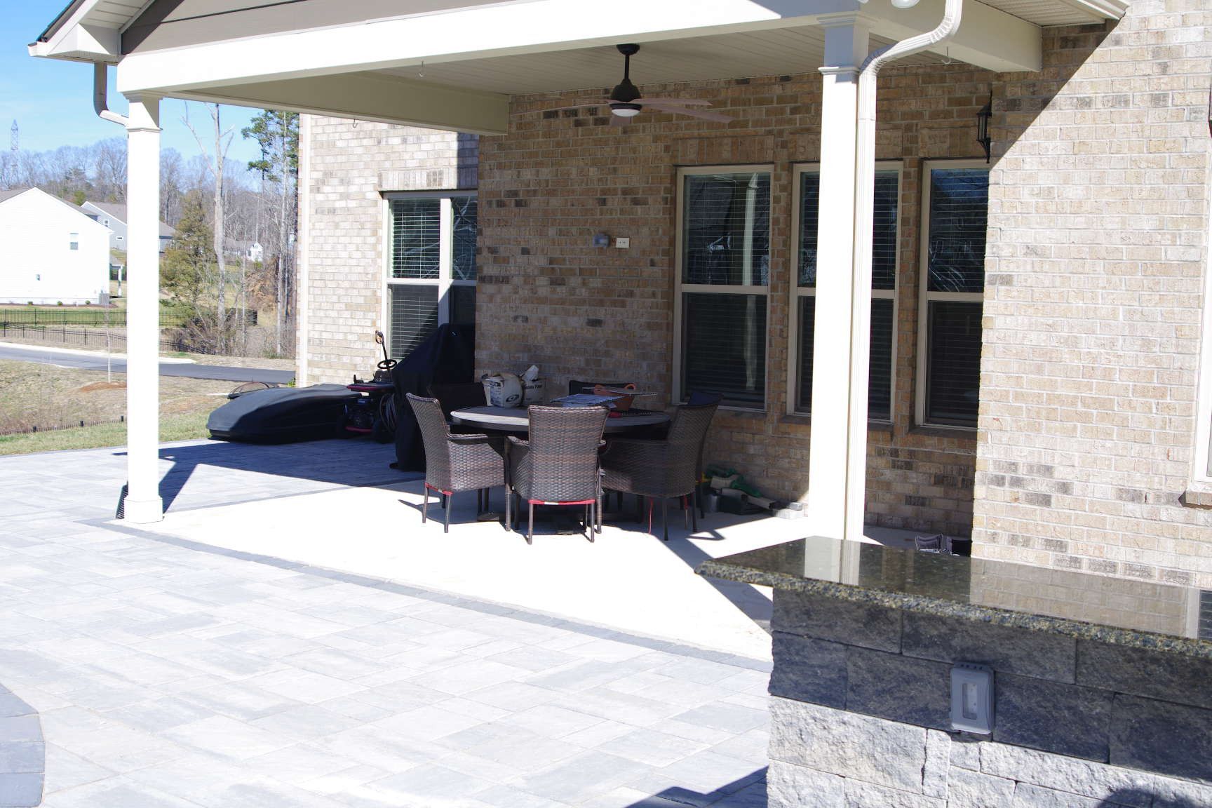 Covered brick patio with outdoor sofa, chairs, and table under a roof overhang