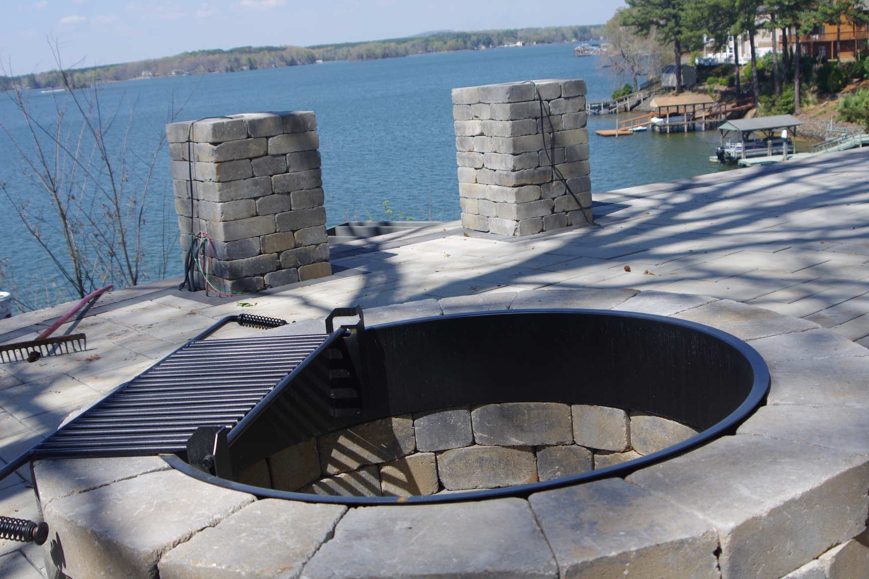 Stone fire pit by a lakeside patio with two stone posts and blue water in the background