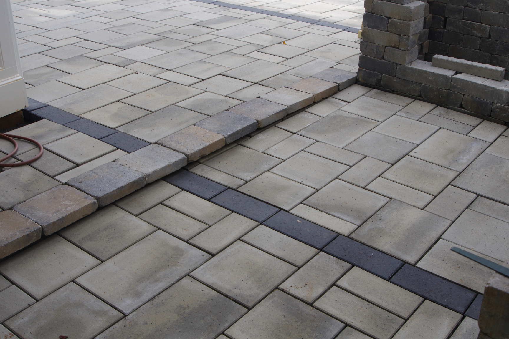 Stone patio with light pavers and dark border strips near a step and wall