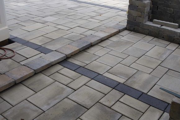 Circular stone planter in a paved patio, with a fence and houses in the background