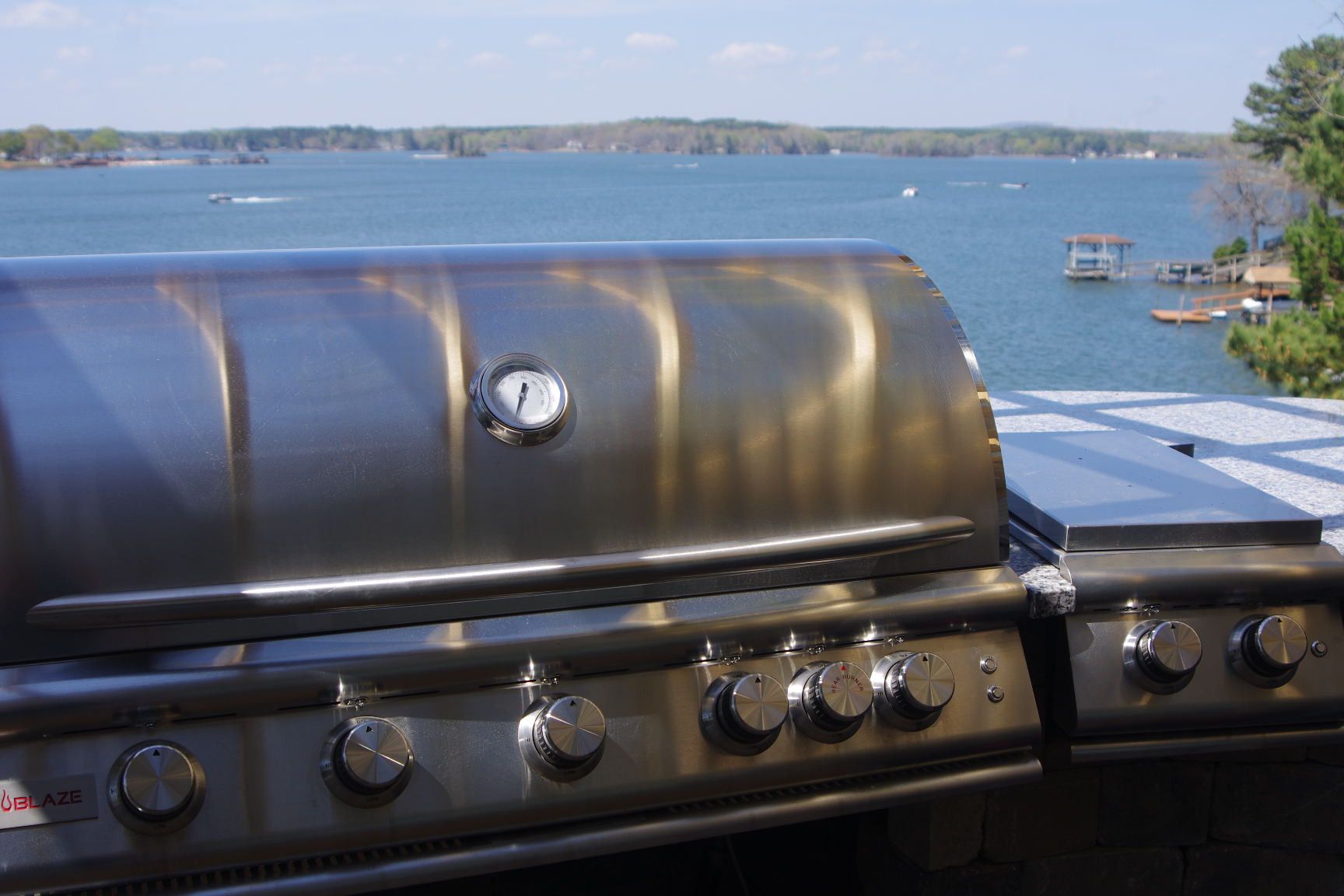 Stainless steel grill on a deck overlooking a calm lake under a clear sky