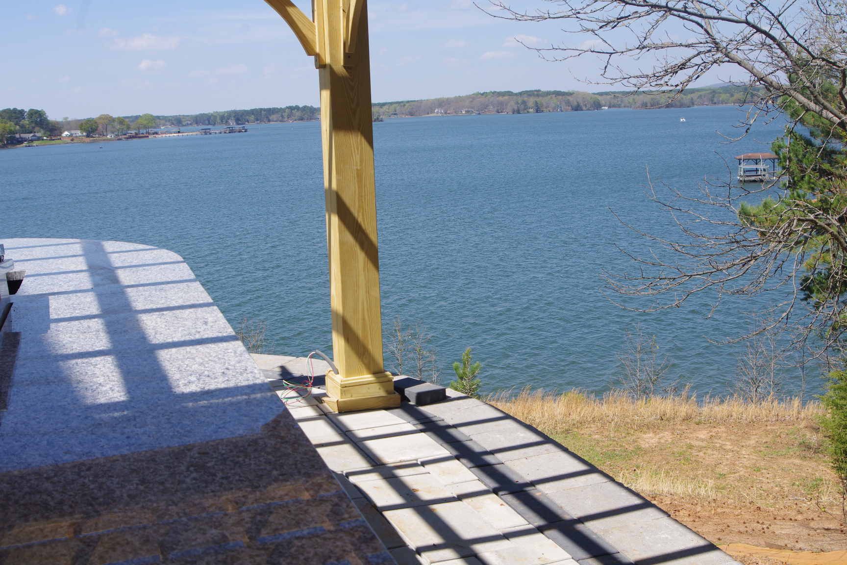 Shaded lakeside patio with wooden post, stone walkway, and view of blue water under a clear sky
