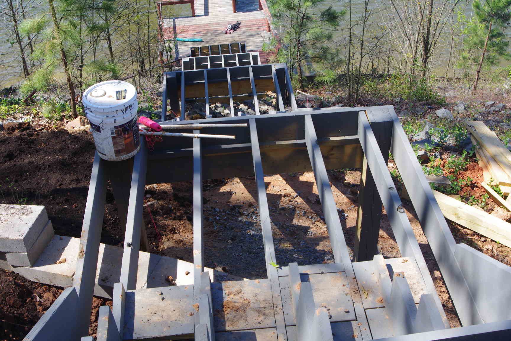 Partially built wooden deck frame with white paint bucket and tools in a yard