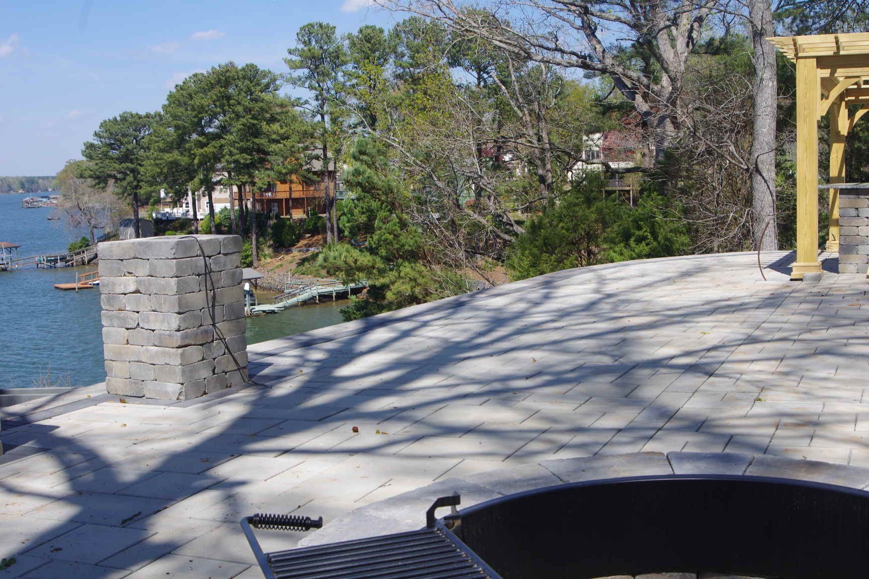 Rooftop patio by the water with trees, a stone chimney, and a yellow railing in sunlight